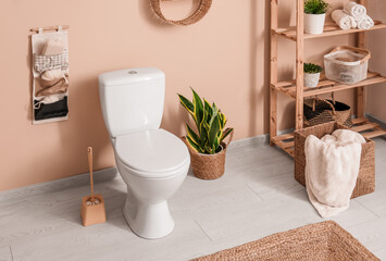 Interior of stylish bathroom with houseplant and ceramic toilet bowl near beige wall - obrazy, fototapety, plakaty