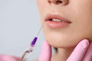 Beautiful woman receiving lip injection on light background, closeup