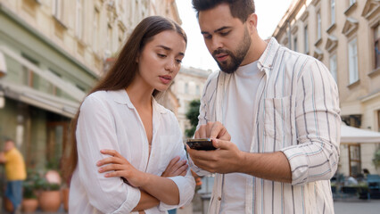 Couple Caucasian man woman using mobile phone smartphone internet maps location tourism trip tour GPS navigation app city center outside street confused male female attractions journey direction urban