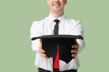 Male student with mortar board on green background