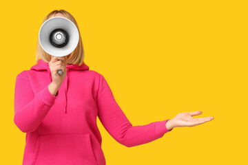 Mature woman with megaphone pointing at something on yellow background - obrazy, fototapety, plakaty