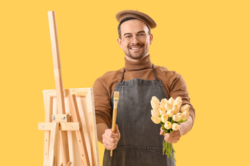 Happy male artist with easel and bouquet of tulips on yellow background. International Women's Day