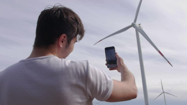 A young guy takes pictures of a wind turbine on his phone