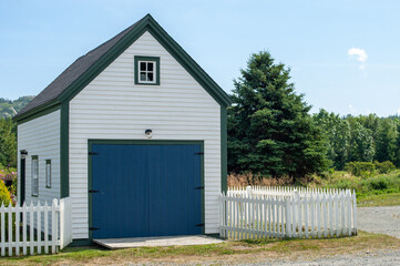 A white and blue single-car garage. The large wooden door on the front of the building is wood....