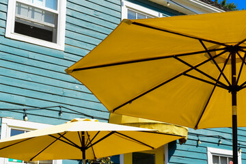 Large summer nylon patio shade umbrellas, yellow in color, opened with brown wooden supports. The...