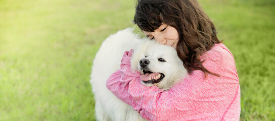 outdoor portrait of young caucasian girl with her pet dog, child owner with white fluffy japanese spitz puppy