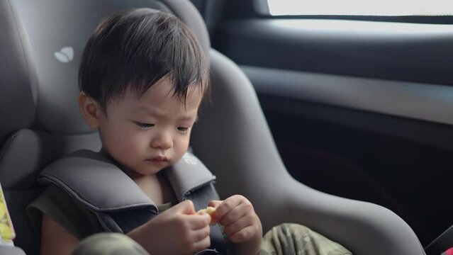 Happy Asian Chinese age 1-2 years old kid enjoying his food while sitting on safety car seat  