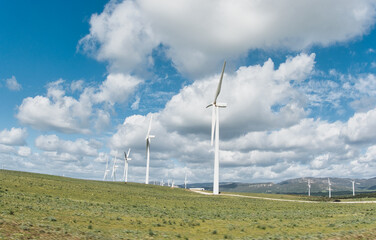 Sustainable energy concept with windmills against a blue cloudy sky spanning rolling green hills