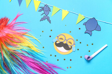 Colorful wig with paper fishes, party whistle and decor on blue background. April Fools Day