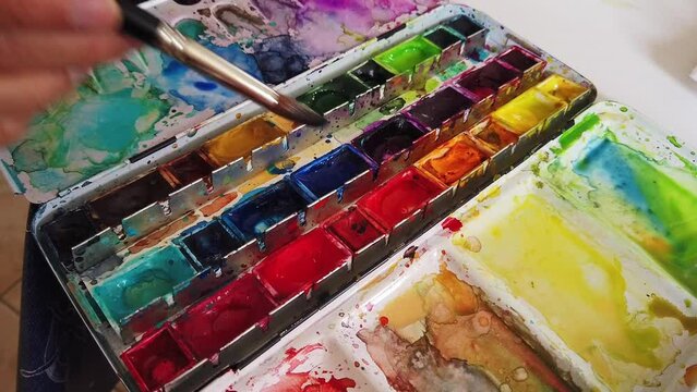 Hand dipping a paint brush in watercolor paint box