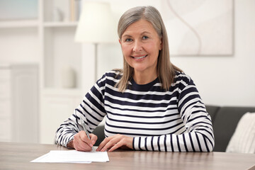 Smiling senior woman signing Last Will and Testament at wooden table indoors