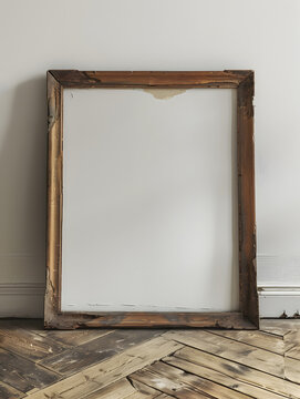A rectangular picture frame with wood stain is displayed on a hardwood flooring next to a plywood wall. It features still life photography under glass, creating a rustic and artistic atmosphere
