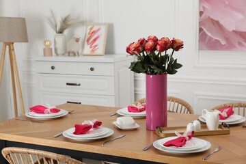 Color accent table setting. Plates, cutlery, pink napkins and vase with beautiful roses in dining...