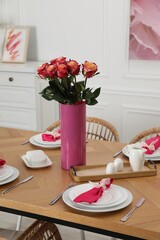 Color accent table setting. Plates, cutlery, pink napkins and vase with beautiful roses in dining...