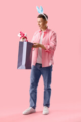 Young man in bunny ears with gnome and shopping bag on pink background. Easter Sale