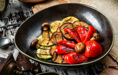 Grilled zucchini, eggplant, bell peppers and mushrooms on plate over wooden background. Vegetarian food, top view