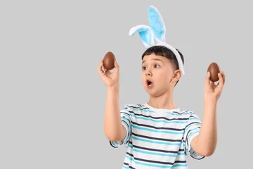 Foto op Canvas Surprised little boy in bunny ears headband with chocolate eggs for Easter on white background © Pixel-Shot