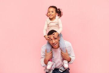 Happy family moments. Cute black little girl sitting on father's shoulders, posing together and...