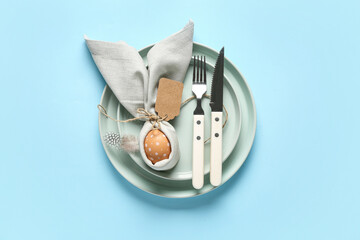 Beautiful table setting with Easter egg and feather on blue background