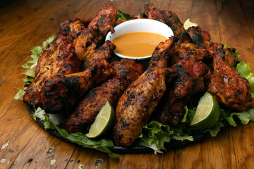 plate of grilled wings on a grill inside a mexican snack bar, with a wooden table and low lighting, with sauce to  to accompany it.