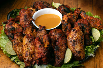 plate of grilled wings on a grill inside a mexican snack bar, with a wooden table and low lighting, with sauce to  to accompany it.