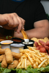 hand of a mexican men holding a potato wedges prepared in a mexican wings bar and snacks, with wooden table and low lighting, with sauce to accompany, holding in her hand a beer in a plastic contai