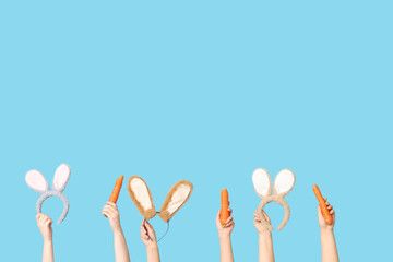 Female hands holding Easter bunny ears headbands and carrots on blue background