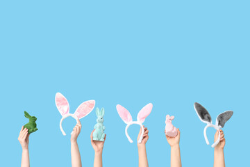 Female hands holding Easter bunny ears headbands and toy rabbits on blue background
