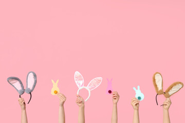 Female hands holding Easter bunny ears headbands and paper rabbits on pink background