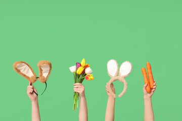 Female hands holding Easter bunny ears headbands with carrots and tulips on green background