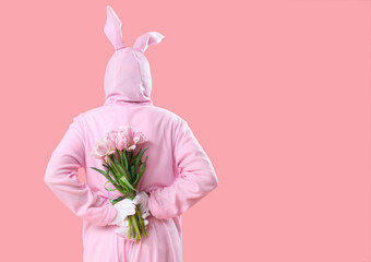 Senior man in Easter bunny costume with bouquet of tulip flowers on pink background, back view