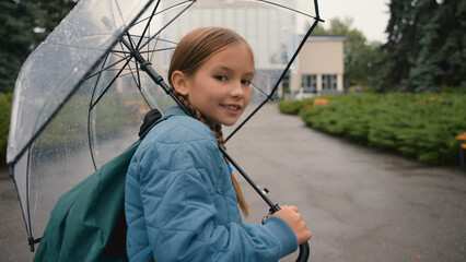 European happy little girl walking city street outside in rain with umbrella back views choolgirl going childhood charming child smile learner school park autumn weather weekend enjoying moving urban