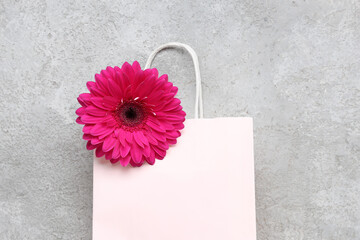 Paper shopping bag with gerbera flower on grey grunge background