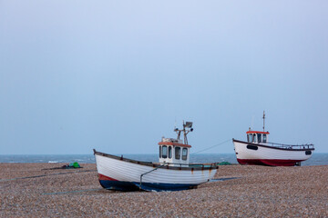 Fototapeta premium Two fishing boats on a shingle beach along the British coast, Image shows a fishing boat in good condition grounded on the beach ready to go out to sea