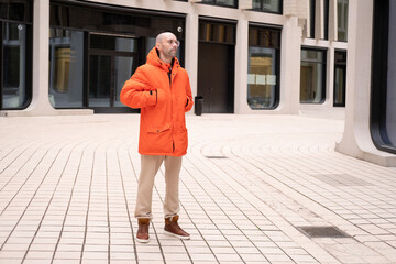 young positive man 30-35 years old man in bright orange jacket with hood on street of Berlin, Youth...