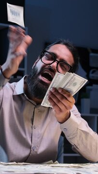 Businessman gleefully makes a rain of cash in the night office. Expressions convey exuberance and celebration, adding a unique and lively touch to the late night work environment.