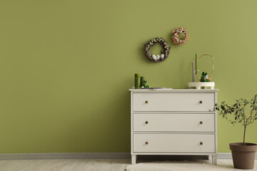 Chest of drawers with candles, bunny and traditional Easter wreaths on wall