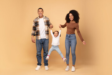 Young loving black parents playing with daughter, holding hands and girl jumping, family posing...