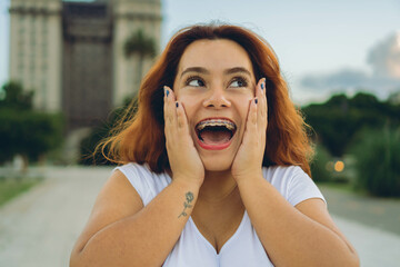young red-haired latin woman in the city makes a surprised expression, with her hands on her face