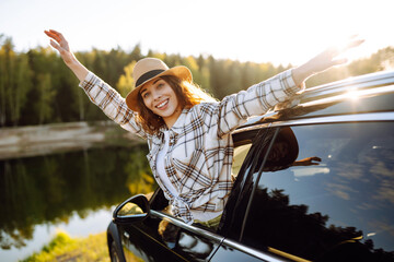 A young woman feels freedom leaning out of a car window in a sunny forest. A traveler enjoys a...