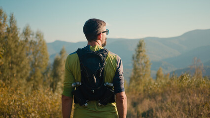 Back view thoughtful calm adult Caucasian male man guy sportsman mountaineer athlete rest hiking looking around enjoy atmosphere sport healthy lifestyle contemplating nature high mountain hill outside - Powered by Adobe