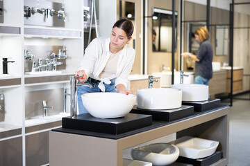 Smiling woman inspects and chooses new kitchen or bath tap faucet at a hardware store