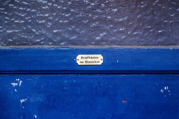 Brass sign on an old blue-painted wooden door with window and the German text Letterboxes in the...