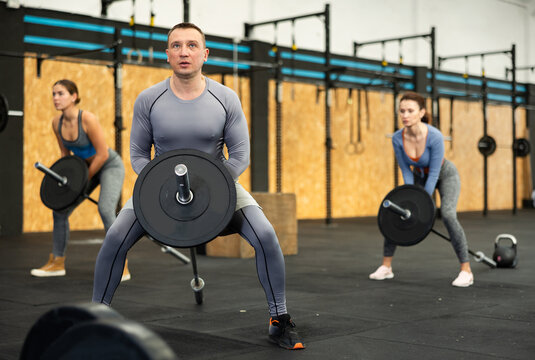 Concentrated middle-aged athletic man engaging in T-Bar row, targeting back muscles, in dynamic gym environment with fitness enthusiasts - Powered by Adobe
