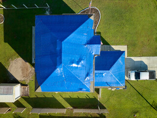 Aerial view of damaged in hurricane Ian house roof covered with blue protective tarp against rain water leaking until replacement of asphalt shingles © bilanol
