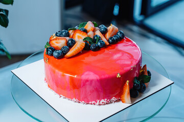 Cake covered in red icing, with strawberries and blueberries.