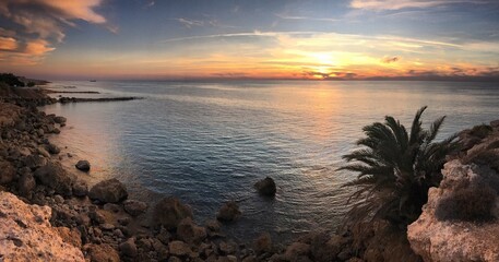 Fototapeta na wymiar Sunset over the rocks and the palm trees on the coast of the Mediterranean Sea near Lémpa, Paphos, Cyprus, October 2018