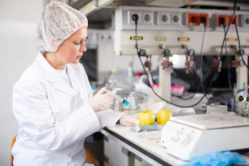 Professional female geneticist working in laboratory, injecting additives into apple during...