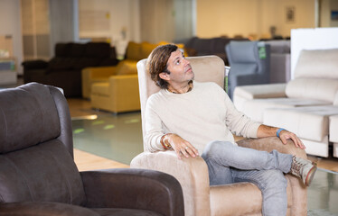 Fototapeta premium positive man is happy to check comfort of chair in shopping center