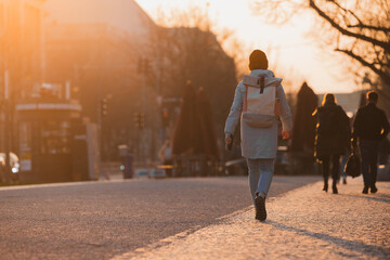 Single woman boldly walking into the sunset on an avenue in berlin. Strong backlight, red and orange color and some lens flare from the low setting sun. Romantic feeling